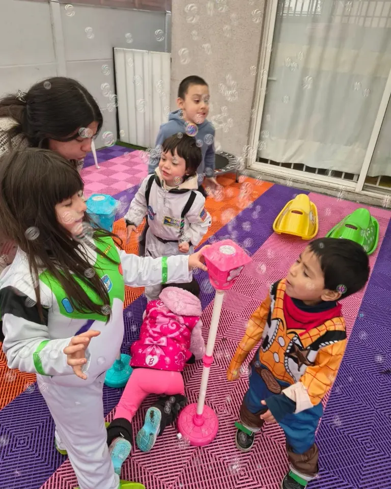 Un grupo de niños juega con burbujas en el patio junto a una educadora