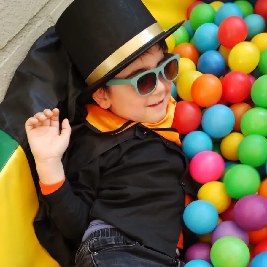 Un niño disfrazado juega recostado en la piscina de pelotas de colores del centro