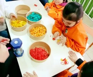 Niñas clasificando fideos de colores en bandejas durante una actividad de mesa