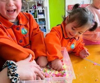 Dos niños comparten una caja de cuentas de colores sobre la mesa